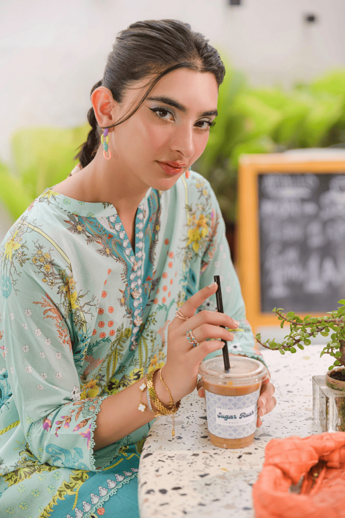 Woman in a floral dress sitting at an outdoor cafe, holding a coffee cup.