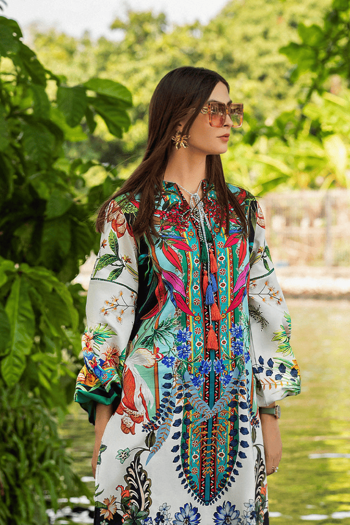 Woman wearing a colorful patterned outfit standing by a body of water with greenery.