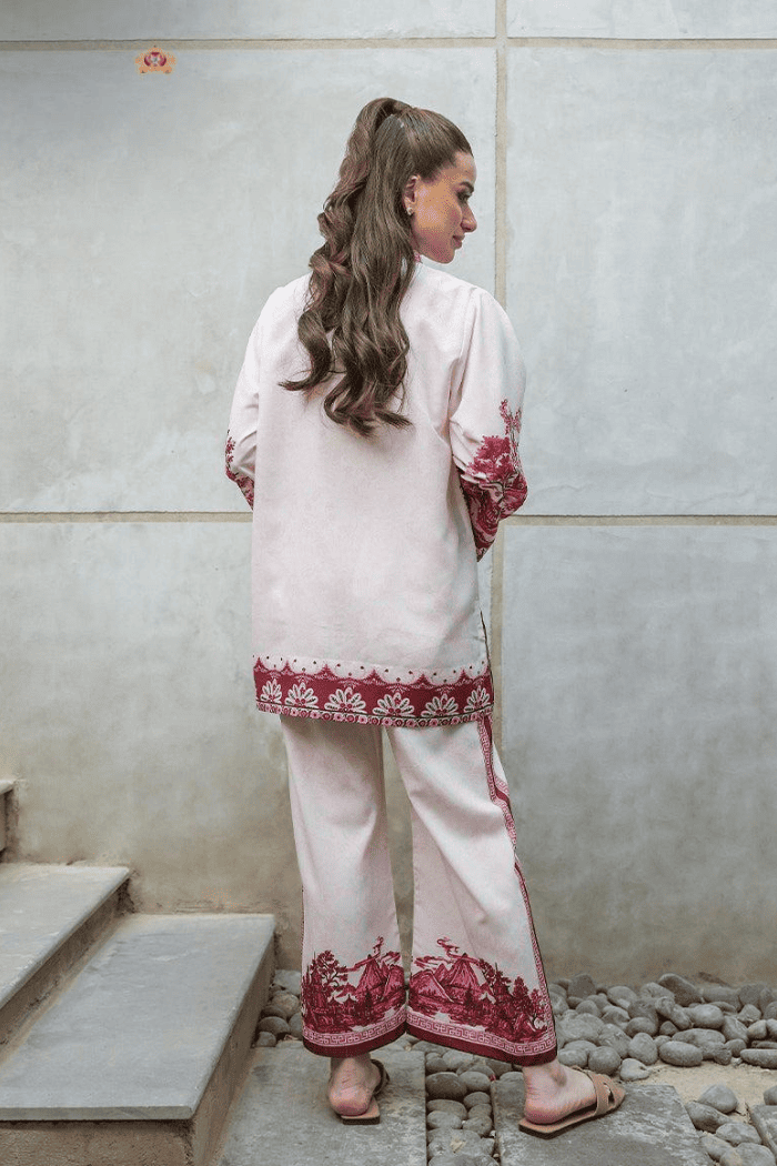 Woman wearing a white outfit with red embroidery standing against a light-colored wall.