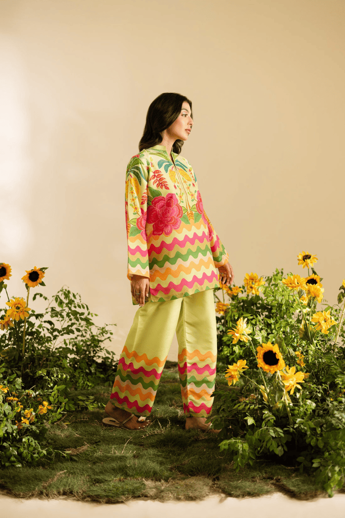Woman in a colorful outfit standing among sunflowers and other flowers.