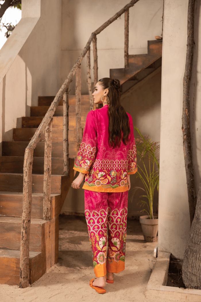 Woman in a vibrant pink traditional outfit standing near a staircase.