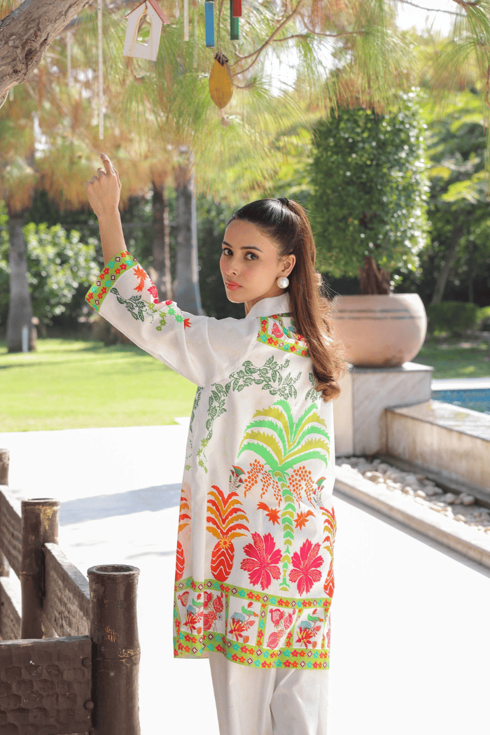 Woman in a colorful traditional outfit standing outdoors with greenery in the background