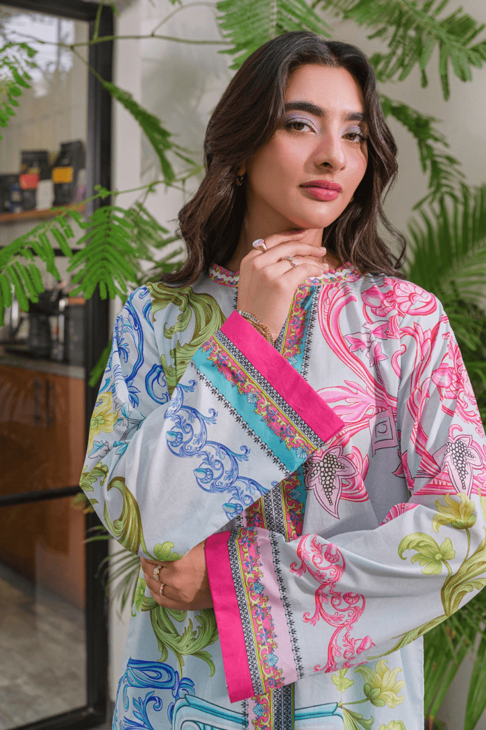 Woman wearing a colorful patterned dress with a pink clutch in an indoor setting with plants.