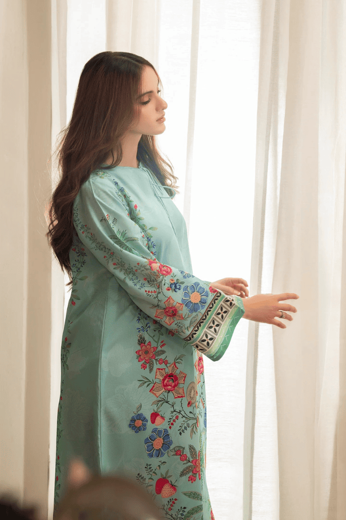 Woman wearing a light blue embroidered dress standing in front of white curtains.
