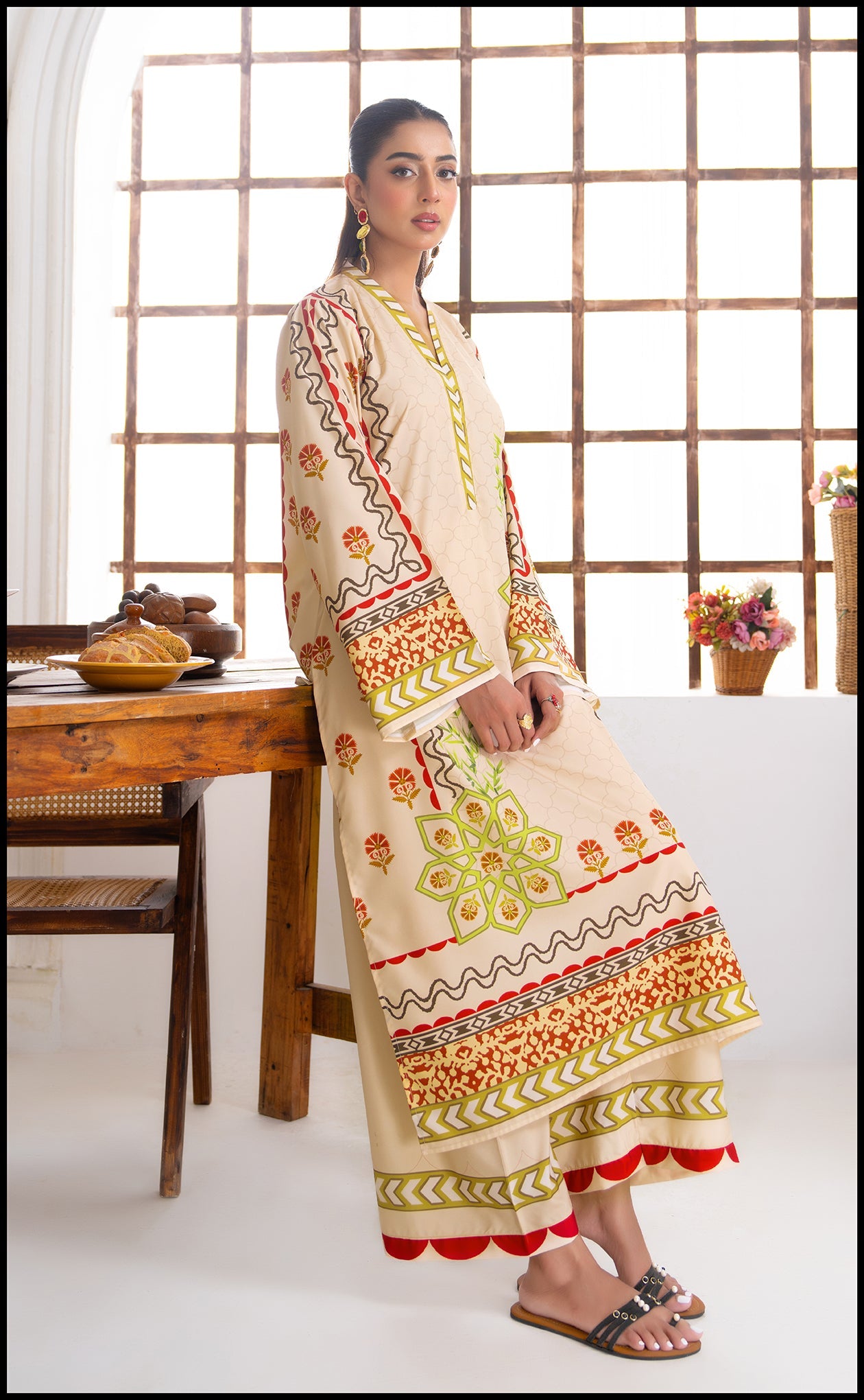 Woman wearing a traditional outfit in a bright room with wooden furniture and decorative items.