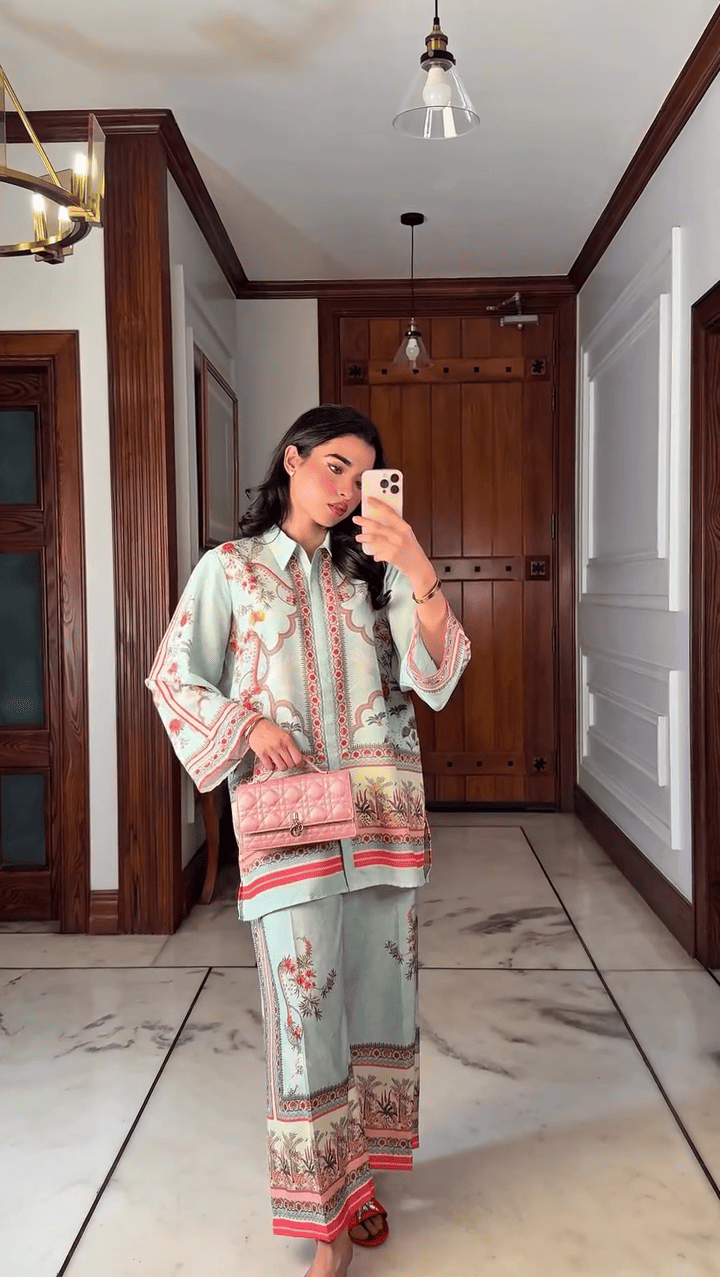 Woman taking a mirror selfie wearing a traditional outfit with floral patterns in a hallway.
